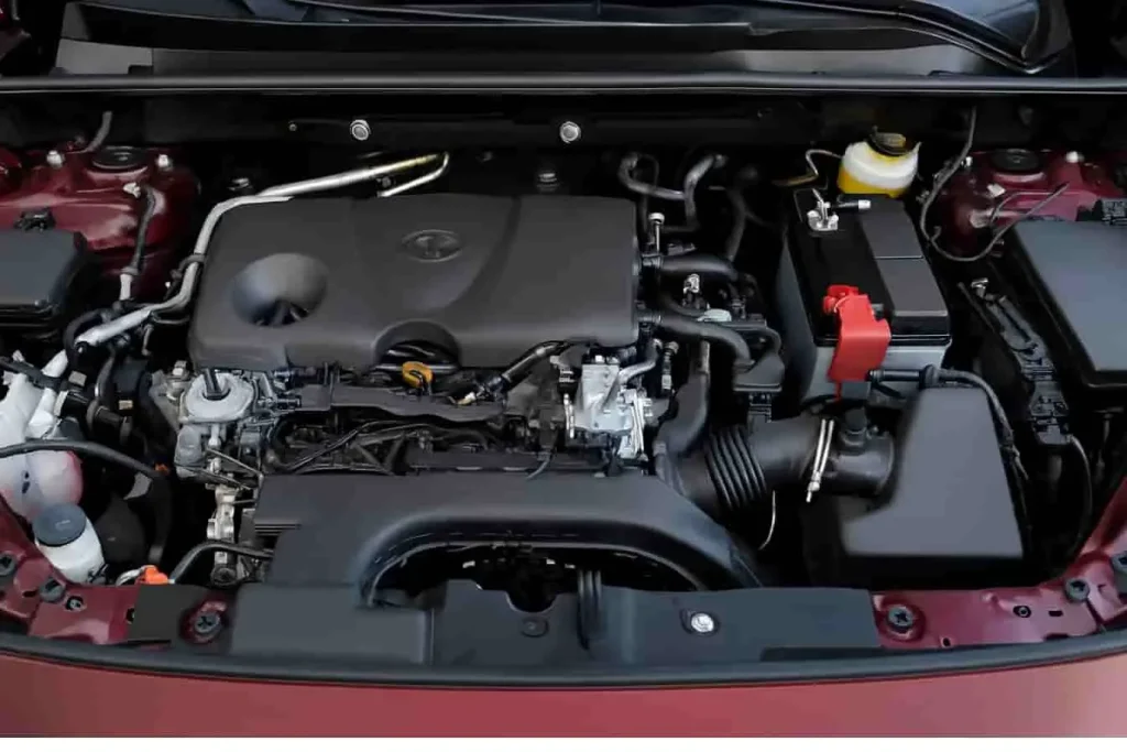 Moteur Toyota RAV4 avec cache gris, batterie orange et durites visibles, image d’un agencement technique précis.