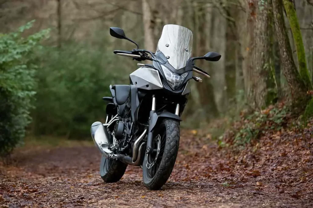 Honda CB500X gris sur piste boisée, moto trail robuste et maniable, idéale pour les escapades en forêt et les trajets du quotidien.