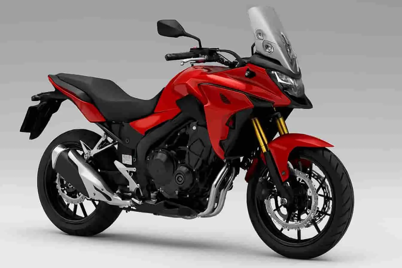 Honda CB500X Moto Honda CB500X rouge, vue trois-quarts, avec pare-brise, fourche inversée dorée et moteur apparent, idéale pour la route et l’exploration.