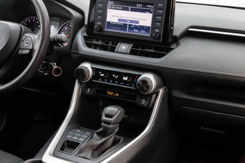 Toyota RAV4 modèle récent, intérieur avec écran tactile, volant à boutons, radio FM et commandes de climatisation.