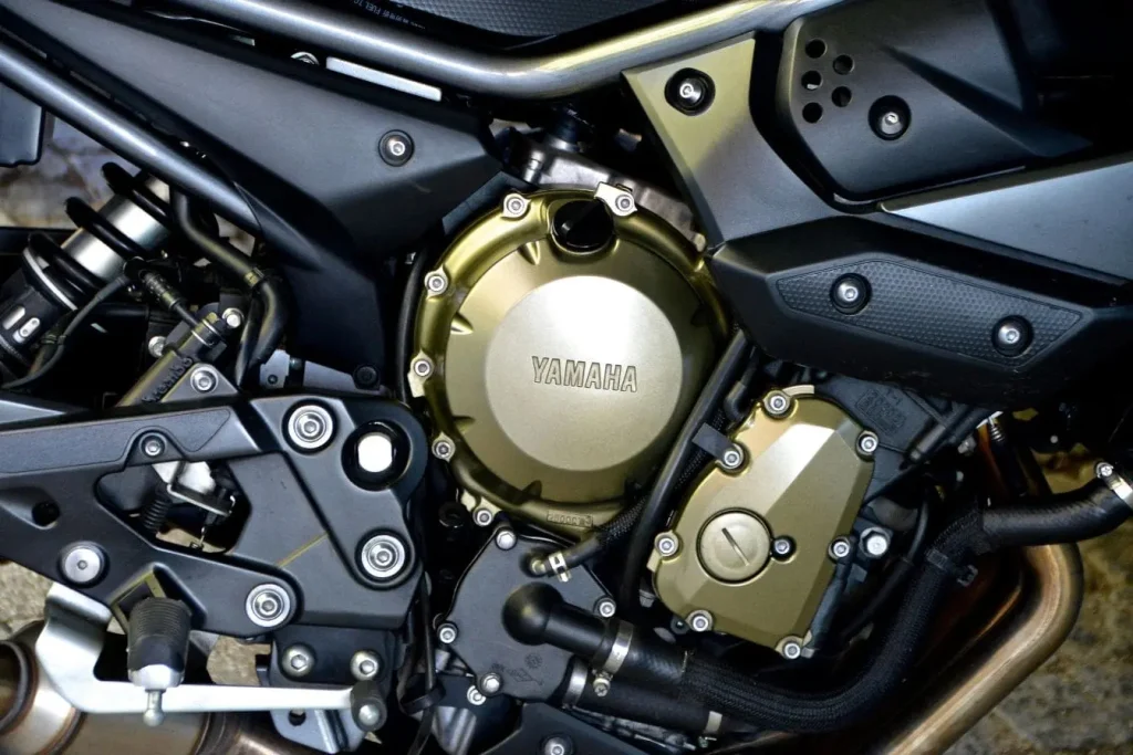 Moteur Yamaha TZR 50 en gros plan, logo gravé sur le carter doré entouré de composants mécaniques.