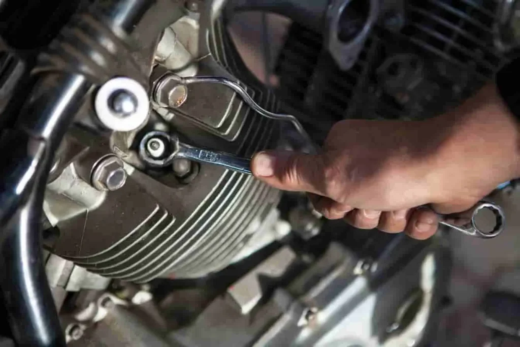 Entretien Honda 500 CX : une main ajuste un boulon sur le moteur à l’aide d’une clé, geste précis sur le côté du moteur.