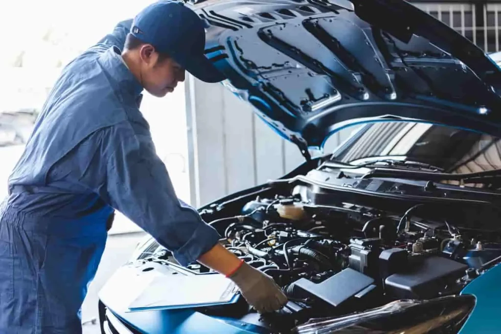 Mécanicien inspectant un moteur 1.3 TCe 140 sous le capot ouvert d’une voiture bleue, en atelier. Entretien ou diagnostic en cours.