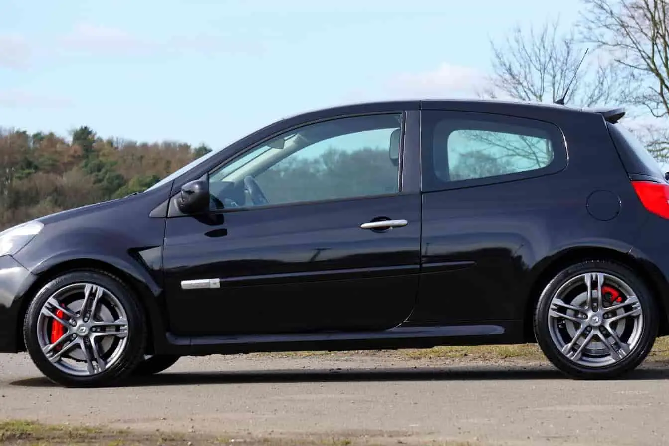 renault clio 5 Clio 5 noire, profil latéral avec jantes rouges et environnement arboré.
