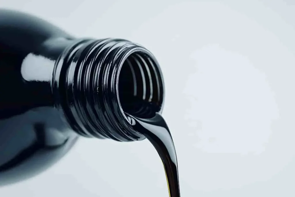 Liquide sombre et épais versé depuis un bidon noir, huile utilisée pour entretenir la direction assistée et garantir une conduite fluide.