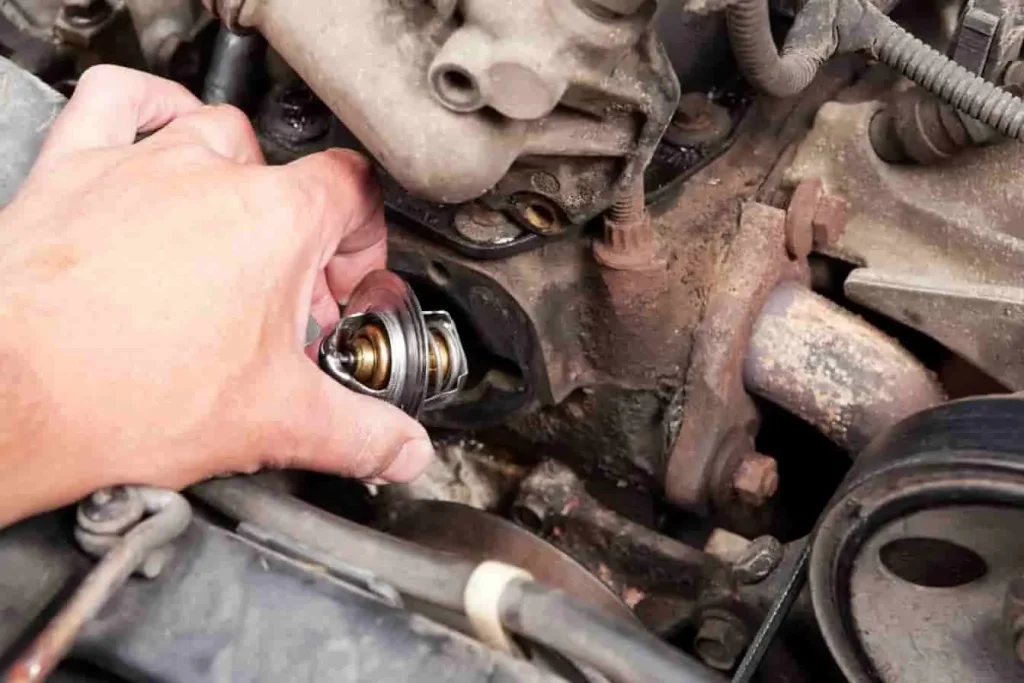 Main installant un calorstat dans le moteur, pièce métallique à capsule de cire, régulant le passage du liquide vers le radiateur.
