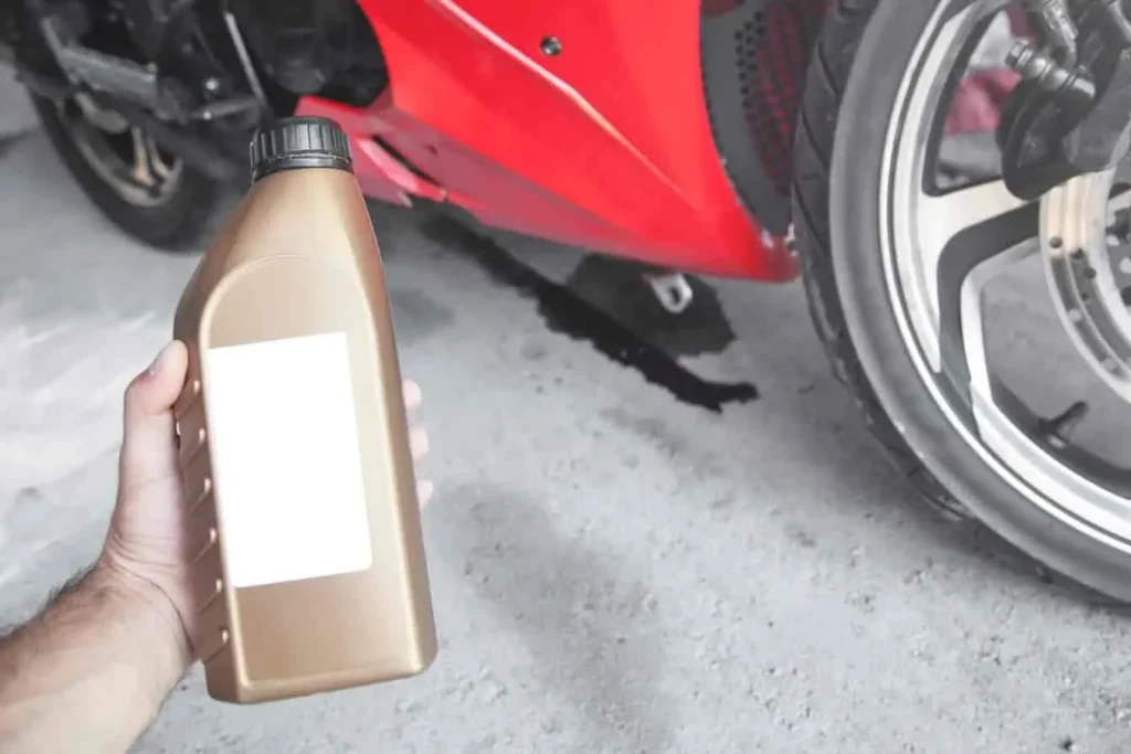 Moto rouge à l’arrêt avec fuite d’huile au sol, bidon à la main, opération de vidange en cours ou à prévoir.