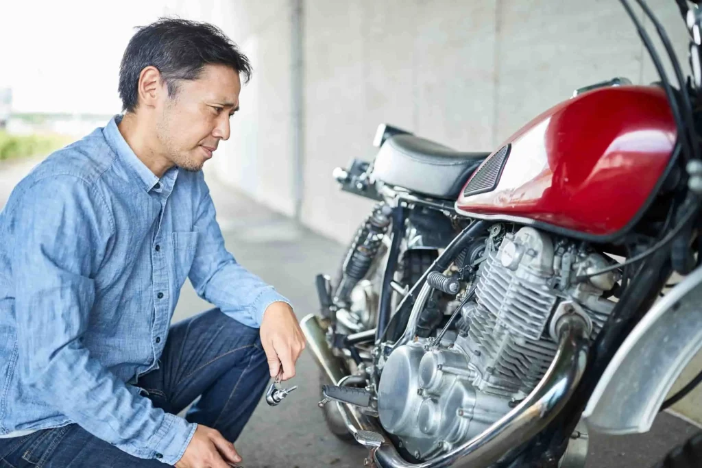 Mécanicien inspectant le moteur d’une moto rouge, étape préparatoire au remplacement de l’embrayage.