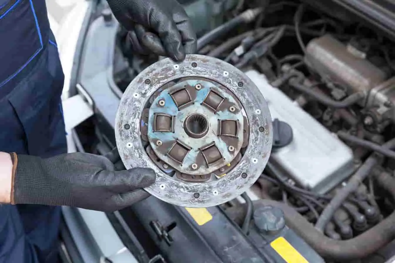 changer un embrayage Une main gantée tient un disque d’embrayage usé au-dessus du moteur, image d’un remplacement en cours après perte d’adhérence