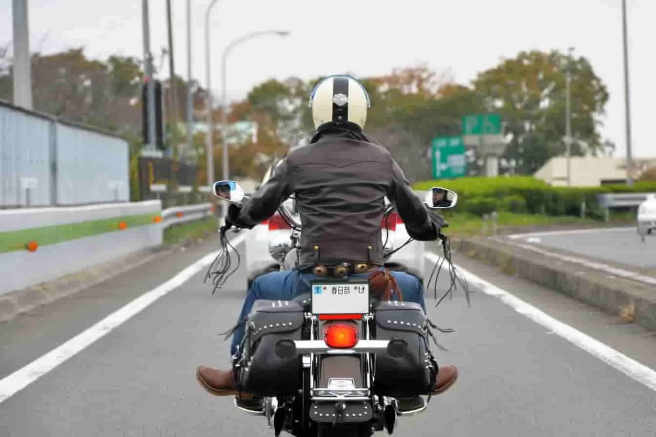 conduire une moto Motard en blouson noir et casque blanc roulant sur route à plusieurs voies, image capturant l’élan et la liberté de conduire une moto.