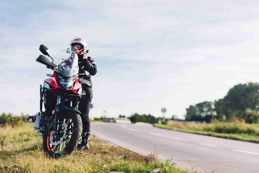 Personne en tenue de motard debout près de sa moto, image évoquant le plaisir de rouler et de s’arrêter au fil du paysage.
