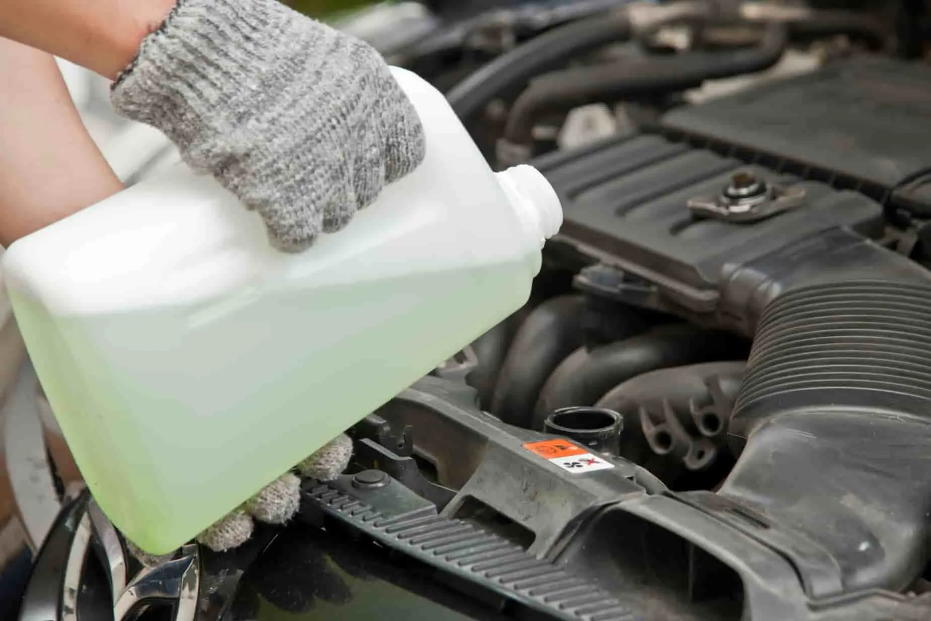 vidanger le liquide de refroidissement Mains gantées versant liquide vert dans le moteur, étape clé pour vidanger le liquide de refroidissement et éviter la surchauffe