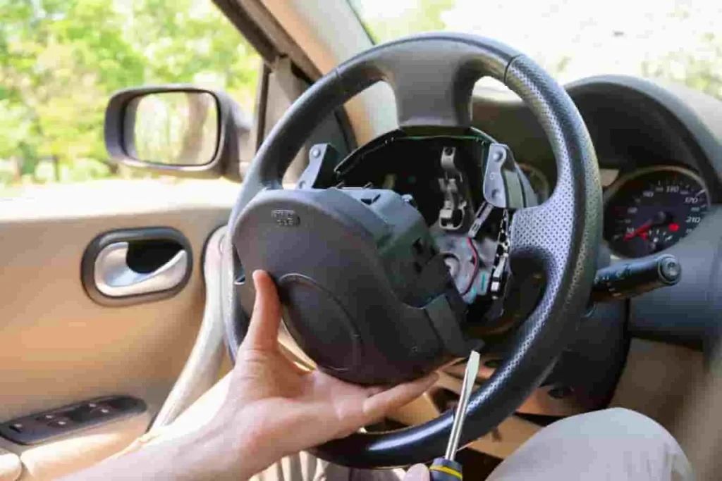 Intervention sur volant avec tournevis, câblage visible, image illustrant le démontage du com2000 dans un habitacle automobile