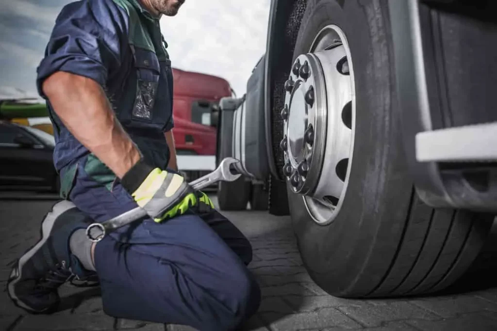 Mécanicien accroupi devant une roue de camion, clé en main, image illustrant l’entretien des pneus pour corriger les vibrations du volant.
