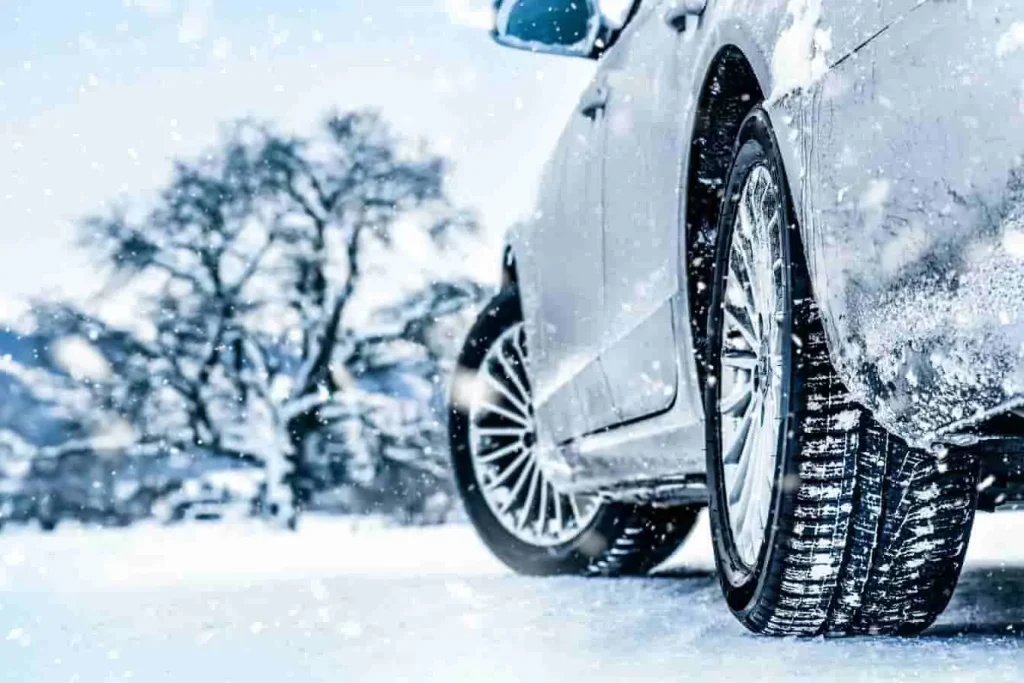 Vue arrière d’un véhicule sur route enneigée, pneu hiver en contact avec la neige, décor de montagne et arbres nus, image d’une sécurité hivernale