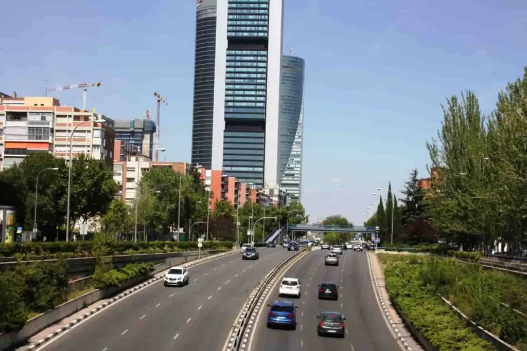Route urbaine avec voitures en mouvement, végétation centrale et gratte-ciels en fond dans une ville soumise à la vignette Crit’Air