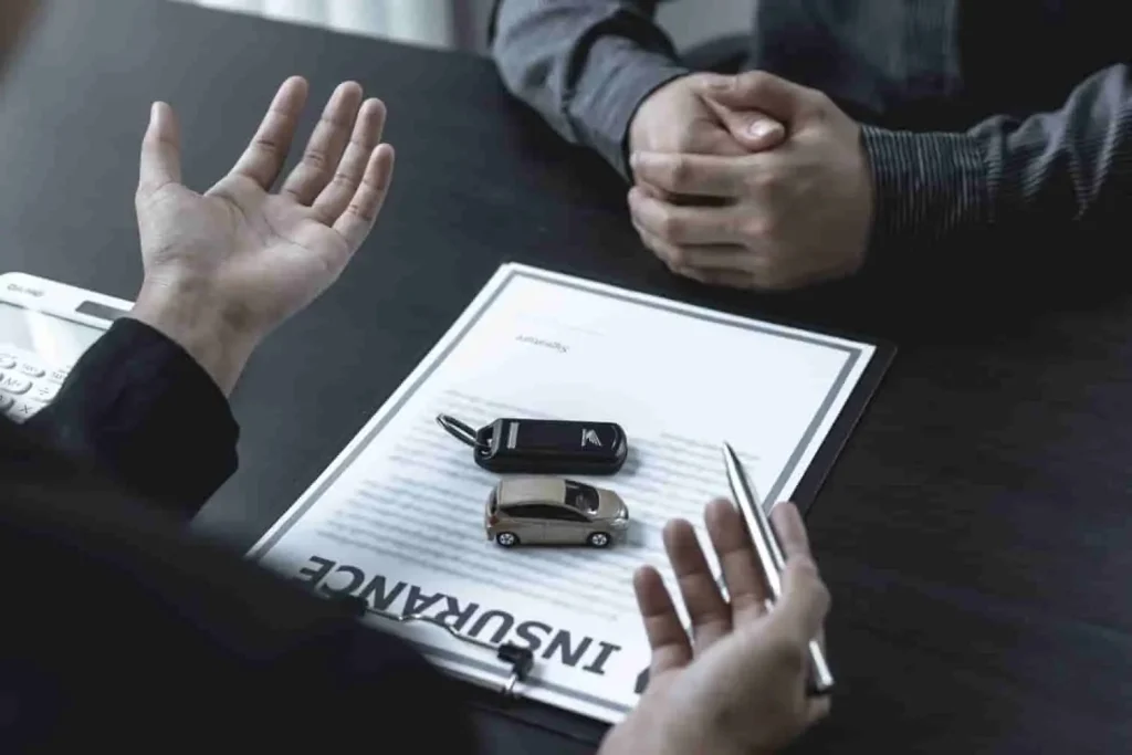 Deux personnes discutent autour d’un contrat d’assurance auto, clé et miniature sur la table, image illustrant une démarche de résiliation.