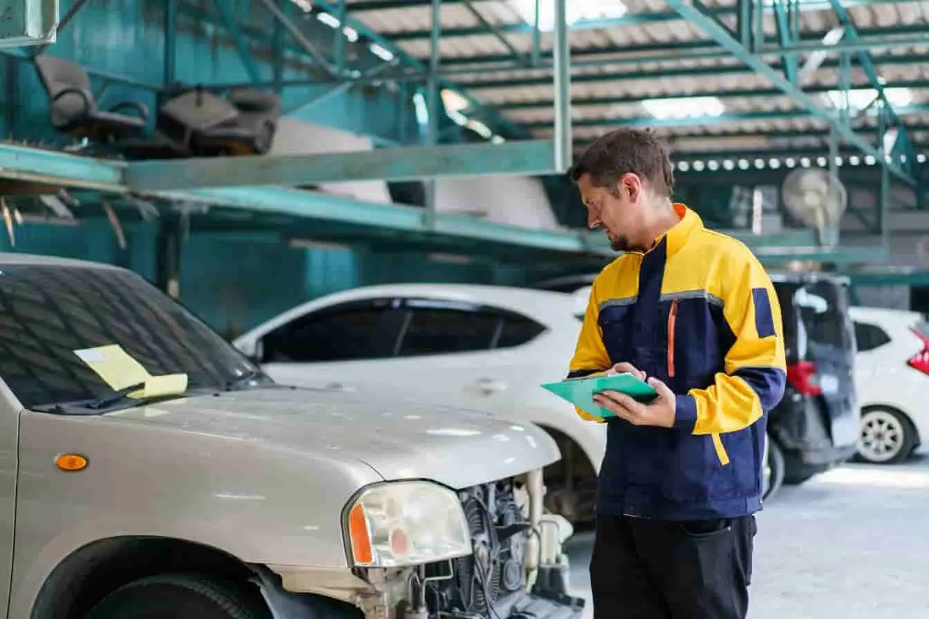 contre-visite voiture Inspecteur en veste jaune et bleue examinant une voiture accidentée dans un garage, image d’une contre-visite après expertise ou réparation