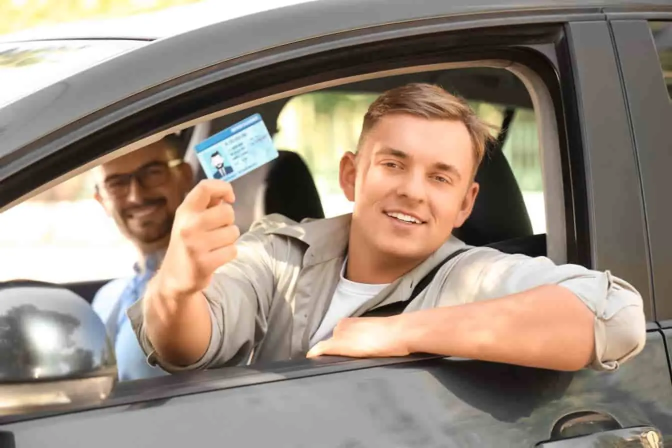 moniteur auto-école Jeune conducteur souriant dans une voiture avec son permis en main, image illustrant la réussite accompagnée par un moniteur auto-école