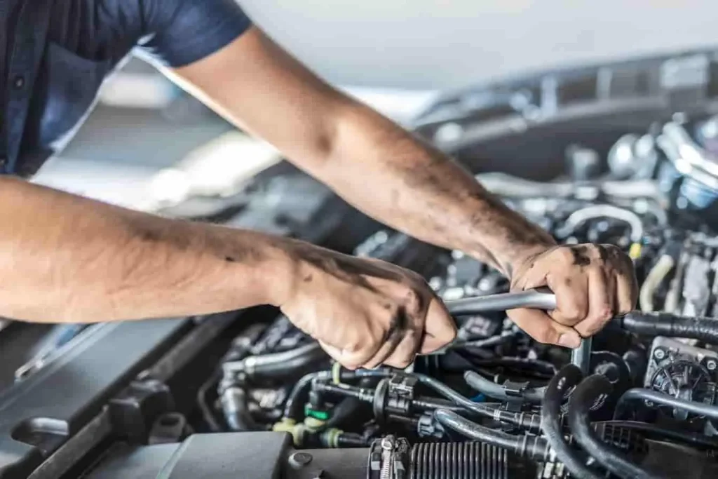 Mains pleines de cambouis travaillant sur moteur, image évoquant une réparation suite à un litige vendeur pour panne moteur