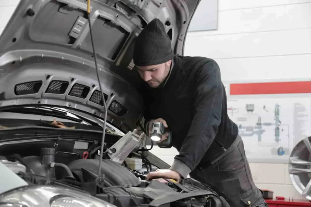 Mécanicien inspectant le moteur d’une voiture dans un garage, lumière à la main, image d’une contre-visite pour valider une réparation technique