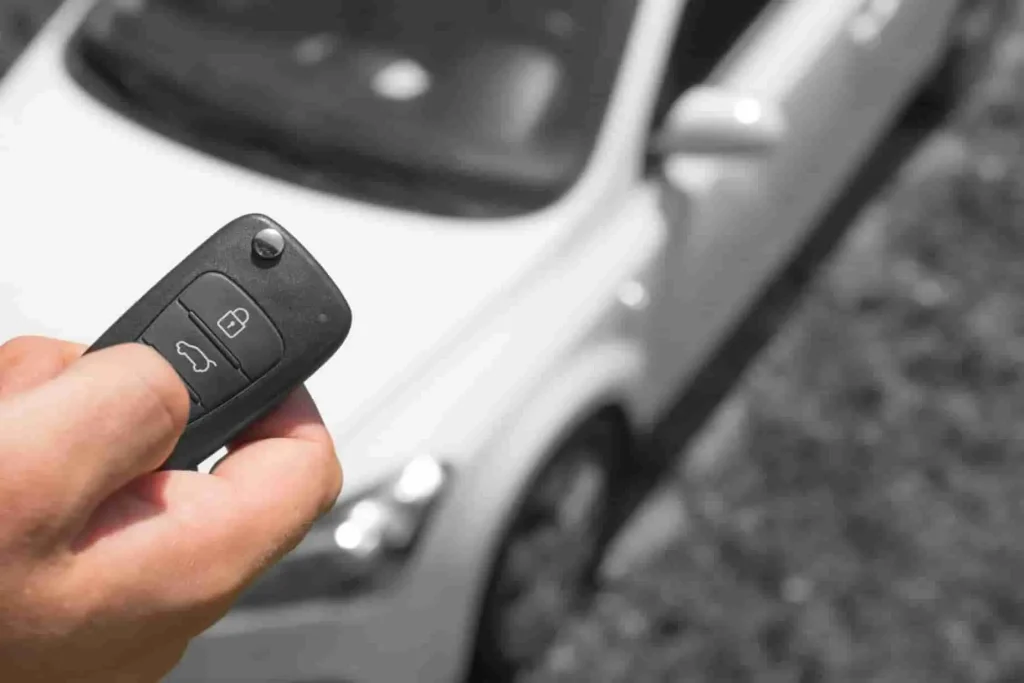 Main tenant une clé télécommande devant une voiture blanche, image qui illustre le rôle du BSI dans le verrouillage centralisé et la gestion des accès