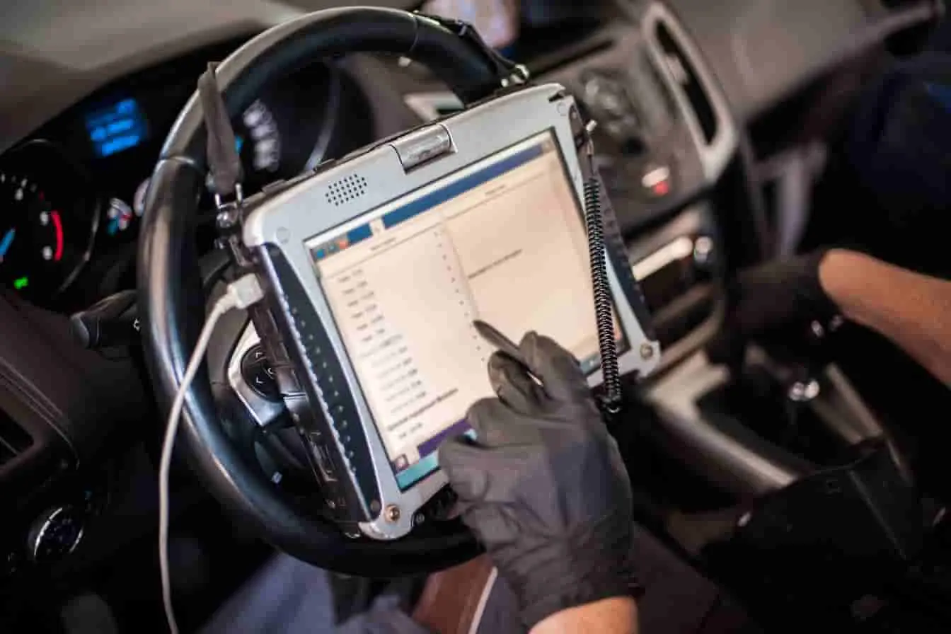 valise de diagnostic Personne utilise une valise de diagnostic posée sur le volant, image d’un contrôle électronique dans l’habitacle du véhicule