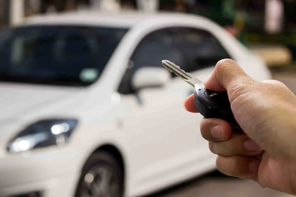 Main tenant une clé de voiture devant un modèle blanc, image qui évoque les enjeux d’accès à la ZFE Grand Paris selon le type de motorisation