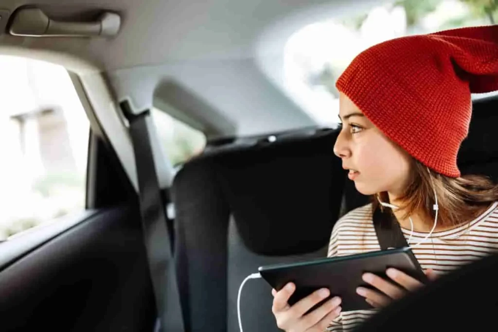 Personne assise à l’arrière d’une voiture avec tablette et écouteurs, image qui évoque une scène de confort numérique liée à Apple CarPlay