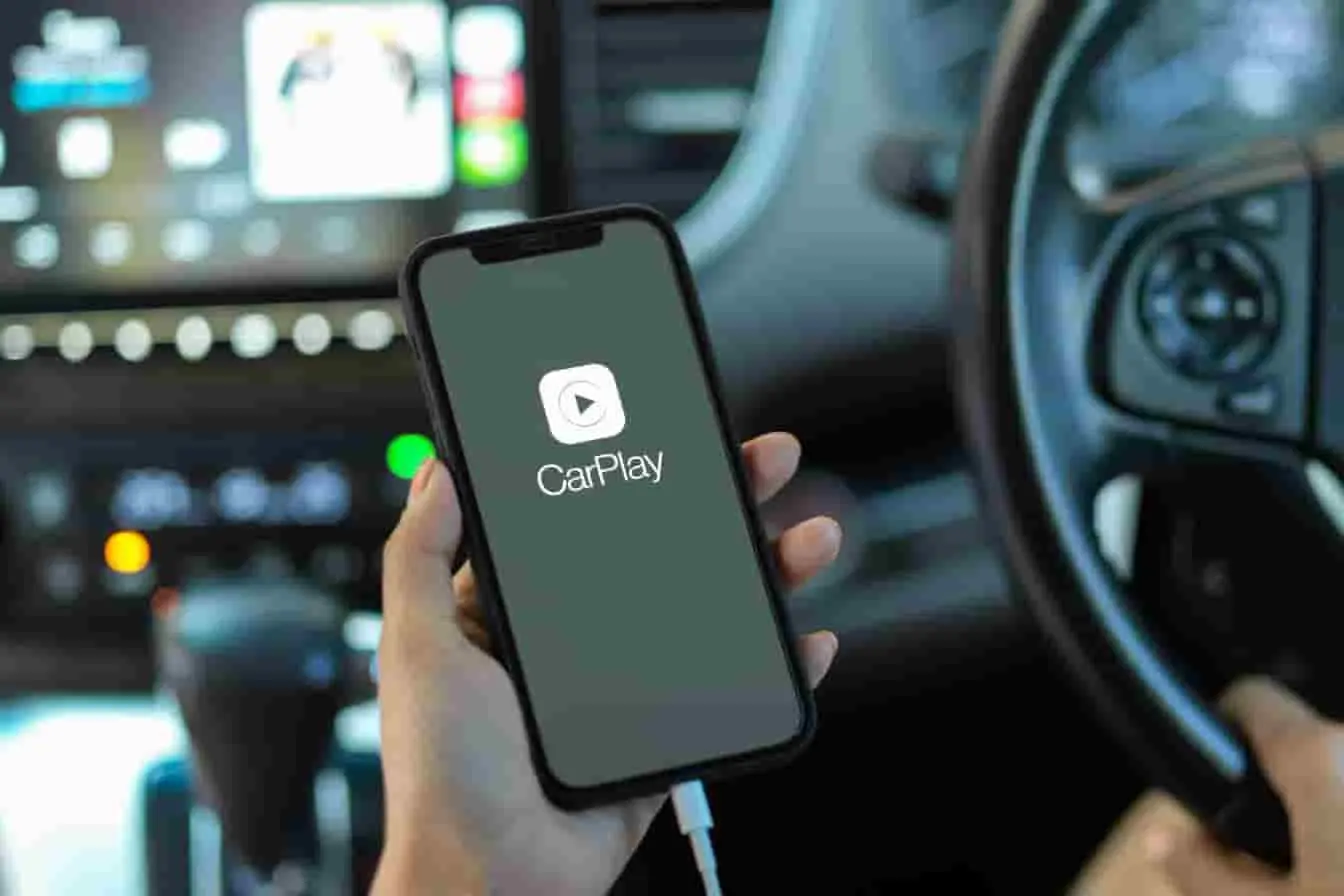 Smartphone affichant CarPlay connecté par câble dans une voiture avec tableau de bord visible, image qui évoque une connexion Apple CarPlay en cours