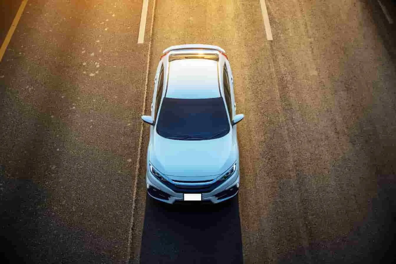 Norme Euro 7 Vue du dessus d'une voiture blanche moderne roulant sur une route au coucher du soleil, symbolisant l'avenir des véhicules neufs face à la Norme Euro 7.