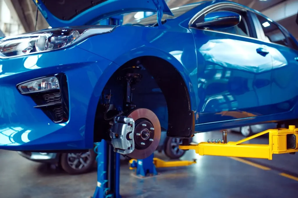 Voiture bleue sur pont élévateur avec roue avant retirée dans garage lumineux, image qui évoque une réparation autonome en libre service