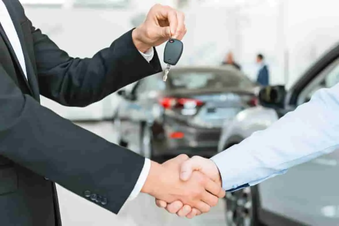 Vente de voiture Deux mains se serrent pendant la remise d’une clé, illustrant la finalisation d’une vente automobile