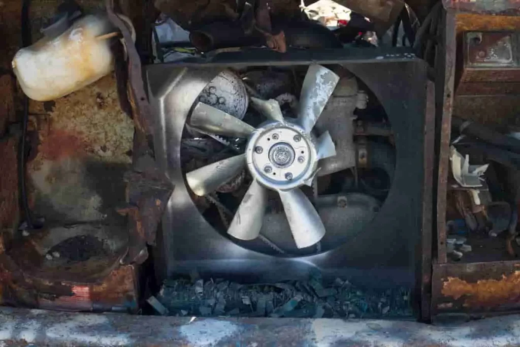Vue rapprochée d’un ventilateur intact au cœur d’un compartiment moteur endommagé, symbole d’un refroidissement qui se poursuit après l’arrêt
