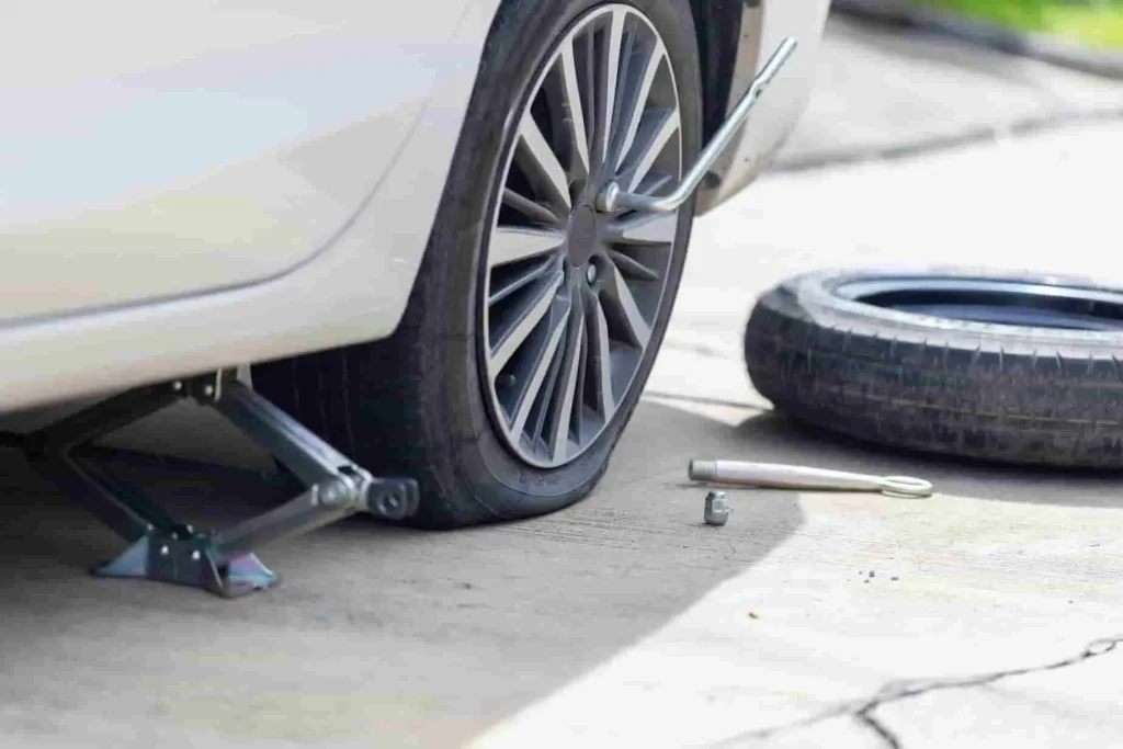 Pneu à plat sur véhicule surélevé avec cric et clé à proximité, image qui reflète une situation nécessitant une solution alternative