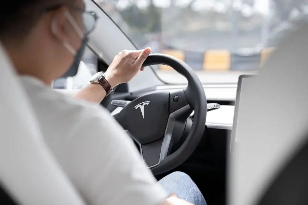 Conducteur assis dans un SUV Tesla tenant le volant avec logo visible, image d’un intérieur moderne et épuré