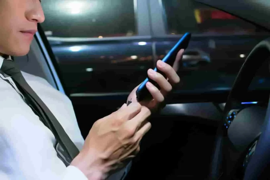 Personne en chemise et cravate assise au volant tenant un téléphone et une cigarette, image qui évoque une interface vocale défaillante en voiture