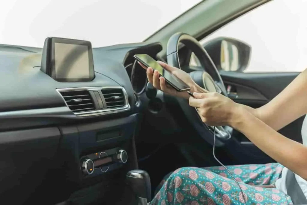 Intérieur de voiture avec écran central et passager manipulant un téléphone branché, image qui reflète une tentative de contournement du bug vocal