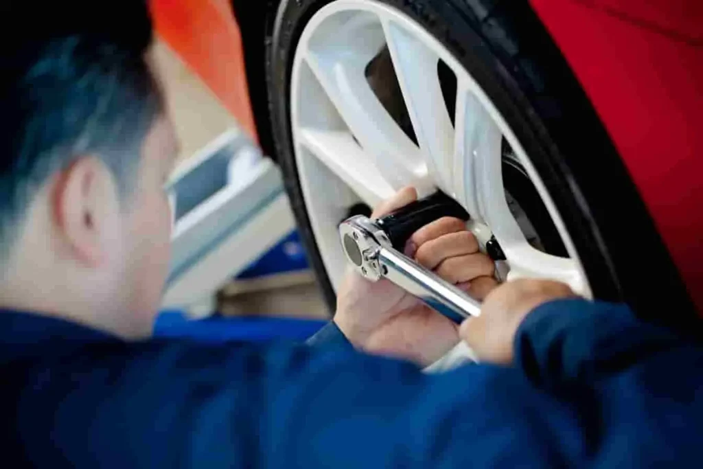 Mécanicien en bleu utilisant une clé dynamométrique sur roue blanche d’une voiture rouge, image qui illustre le serrage précis en atelier