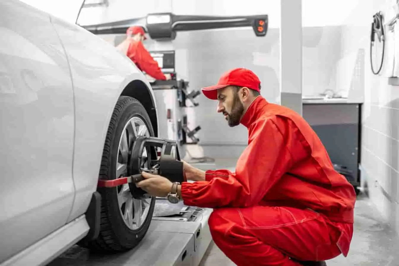 serrage roue voiture Mécanicien en combinaison rouge serrant la roue avant gauche d’une voiture grise avec outil, image qui illustre l’assemblage précis en atelier