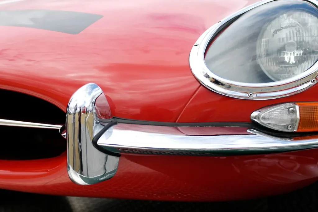 Gros plan sur la face avant d’une Jaguar Type E rouge, image évoquant l’élégance classique en contraste avec le nouveau logo Jaguar