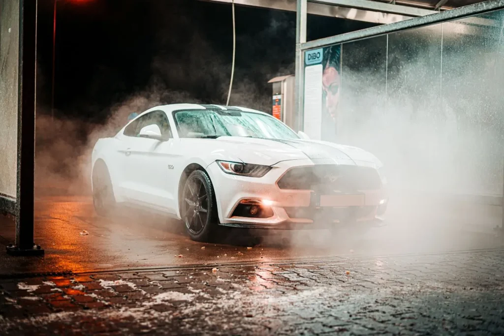 Mustang Mach-E blanche sur sol humide avec brume, image d’un SUV électrique en pleine mise en beauté
