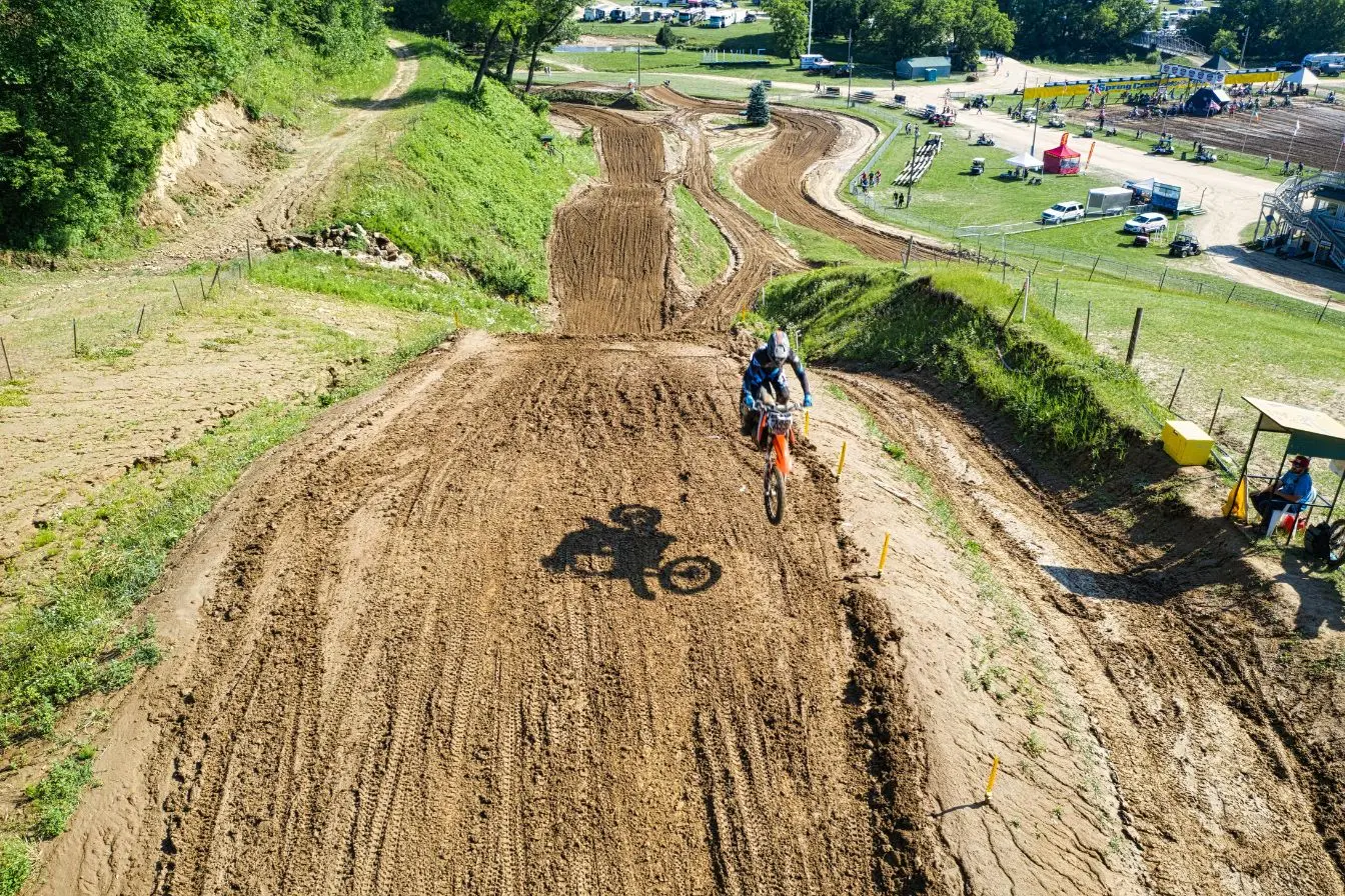Motard en plein saut Motard équipé sur moto orange en plein saut, piste sinueuse et décor naturel typique des trails A2