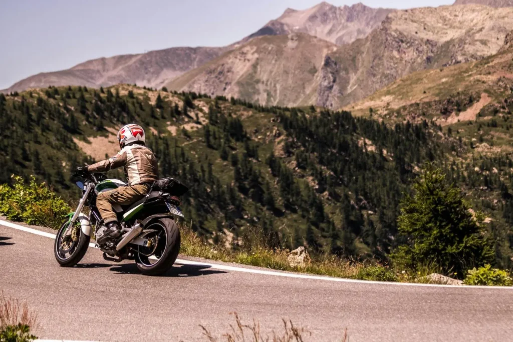 Motard sur route de montagne, casque tricolore et moto verte, virage serré évoquant la Honda Hornet S 600