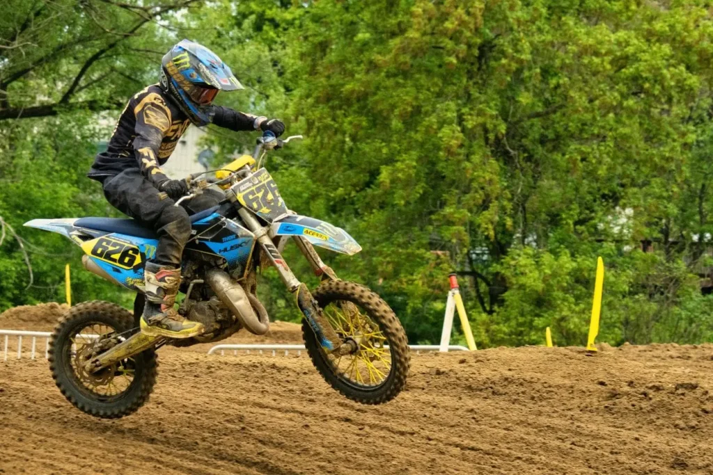 Motard sur moto boueuse capté en plein saut, tenue complète et décor forestier, idéal pour permis A2