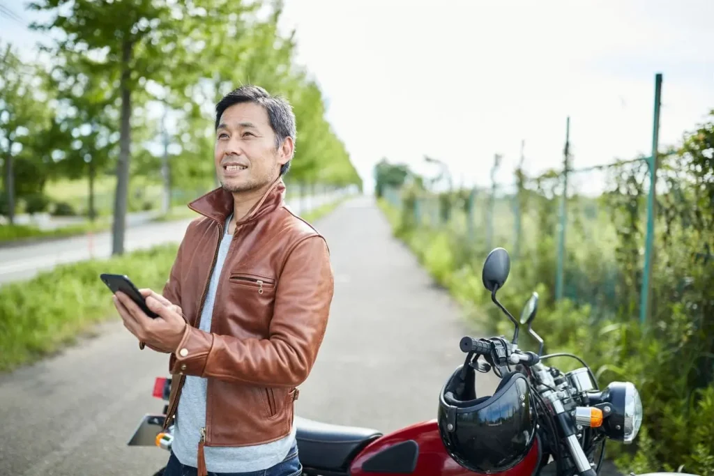 Motard en blouson cuir tenant un smartphone près d’une moto rouge et noire, ambiance vérification avant contrôle