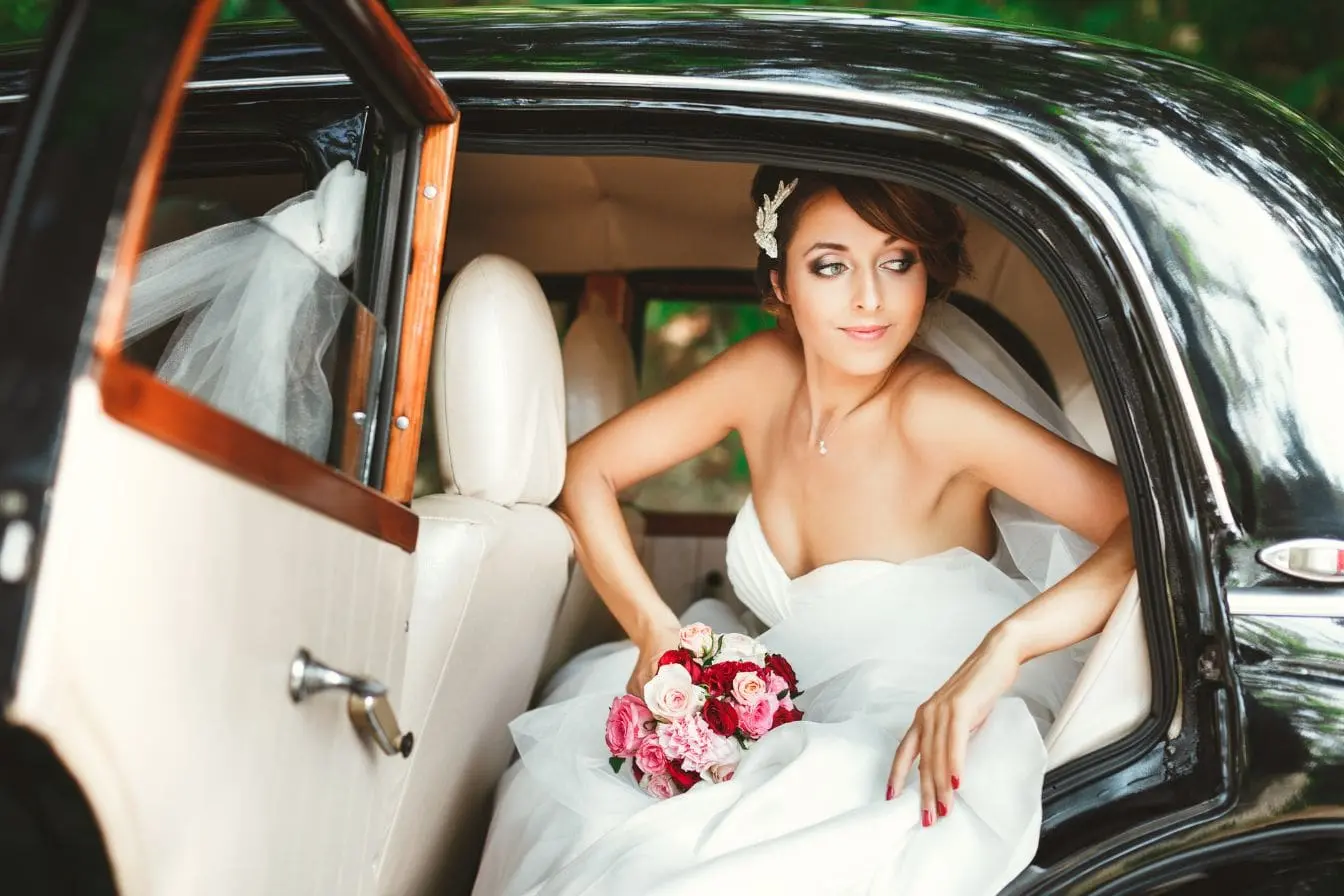 voiture pour mariage Mariée assise dans voiture noire classique, robe blanche et bouquet rose, ambiance élégante évoquant location haut de gamme