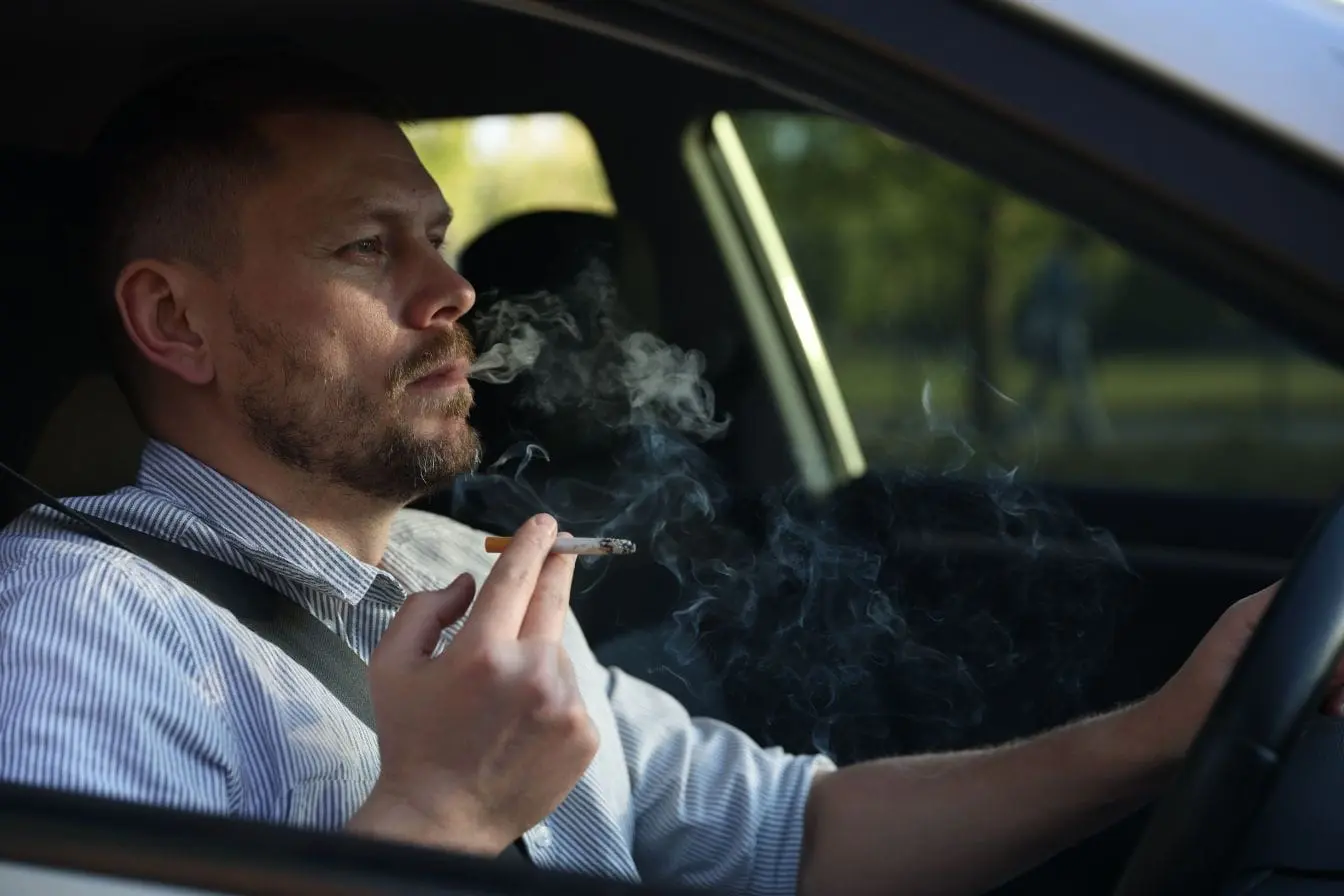 Cigarette allumée Personne fumant dans une voiture illustrant la nécessité d’enlever l’odeur de tabac dans l’habitacle