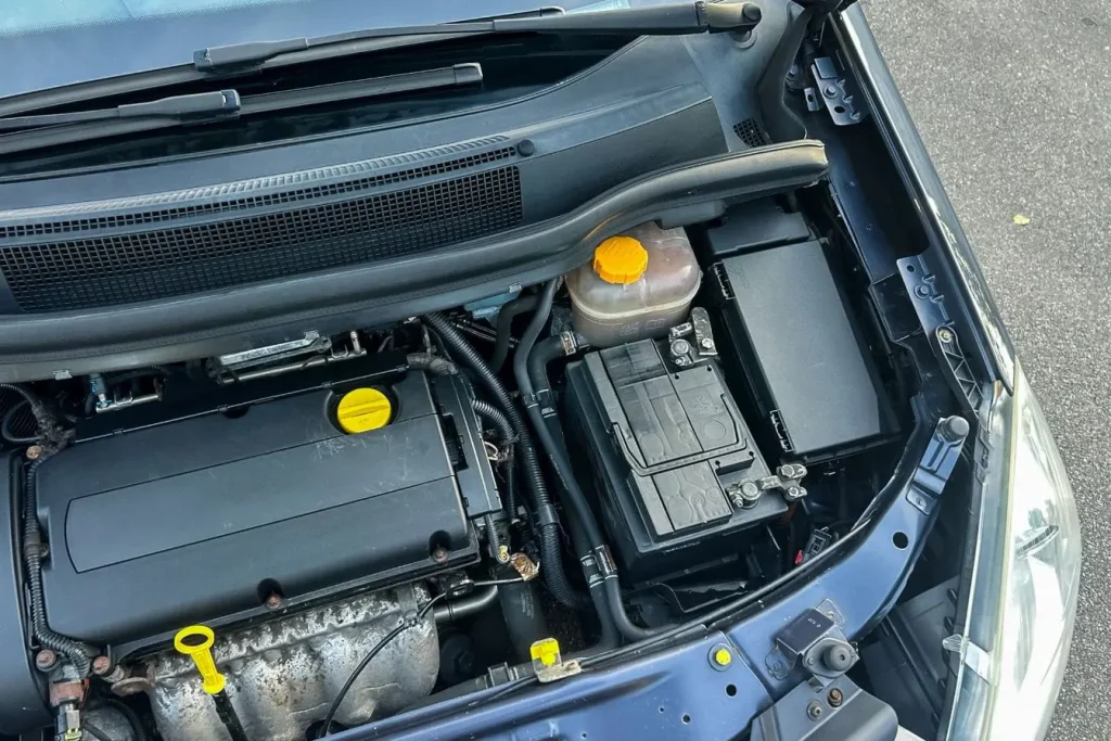 Compartiment moteur ouvert avec batterie visible illustrant une vérification avant branchement d’un booster