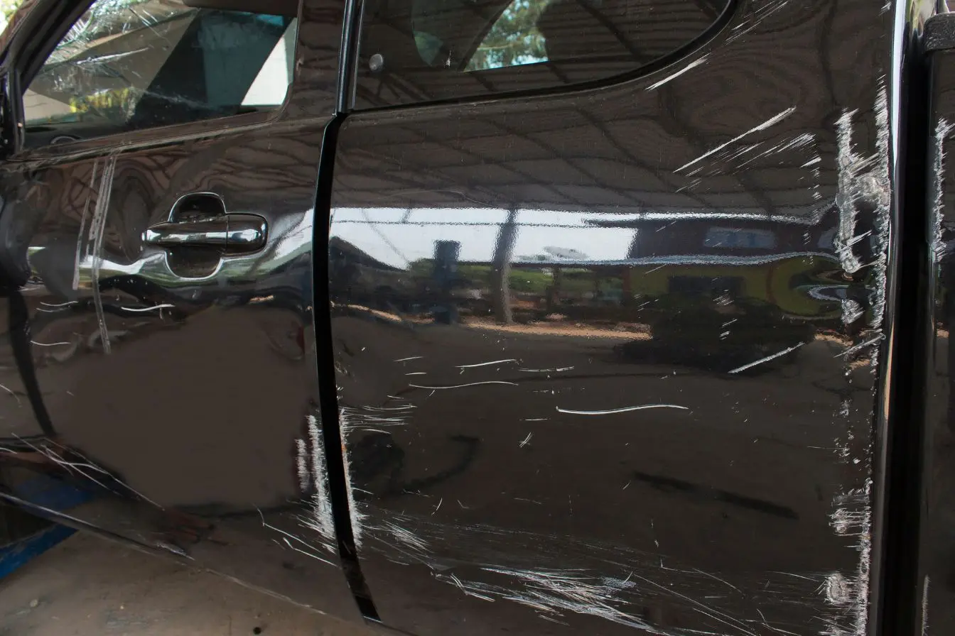 carrosserie rayée Portière noire avec rayures profondes visibles, image d’un dommage à corriger sur la carrosserie